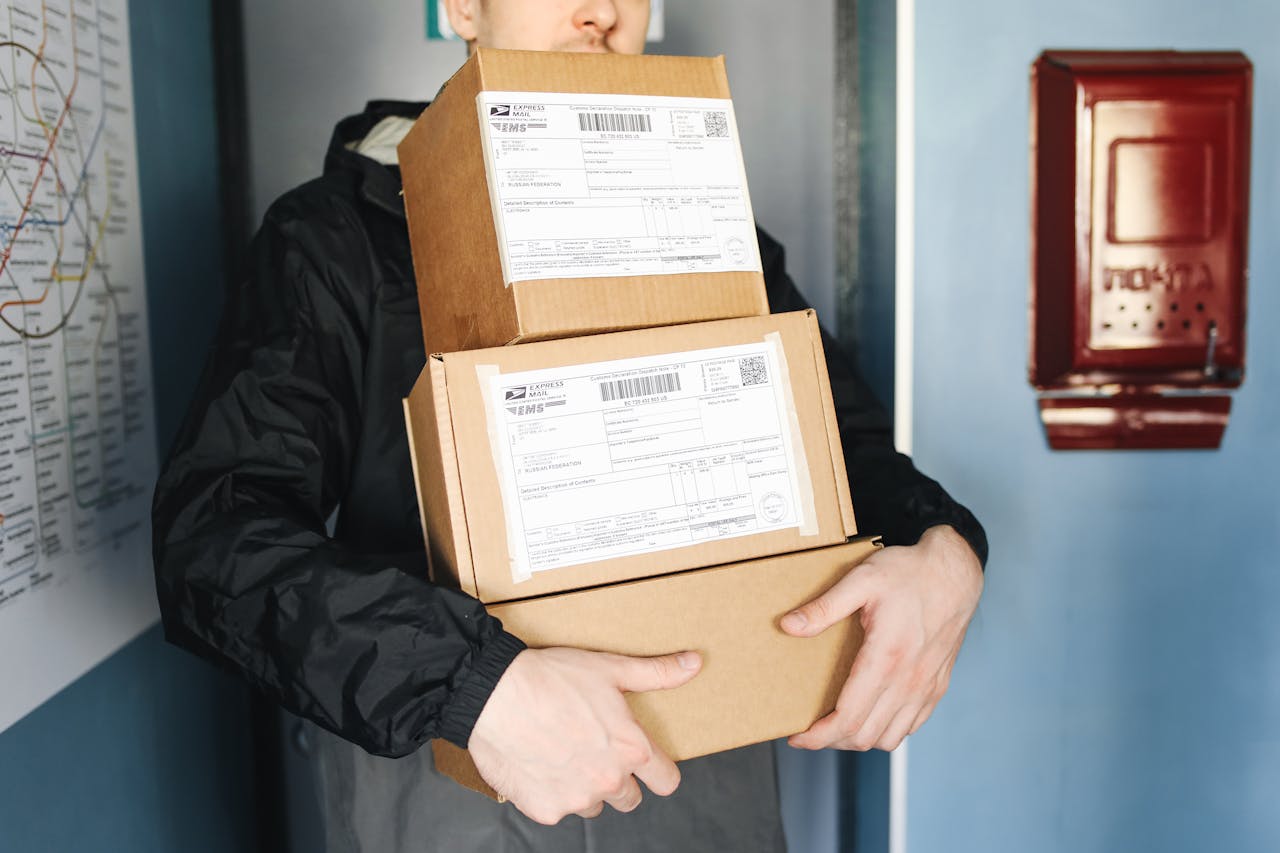 gallery-05 Courier carrying stacked cardboard packages for delivery service indoors.