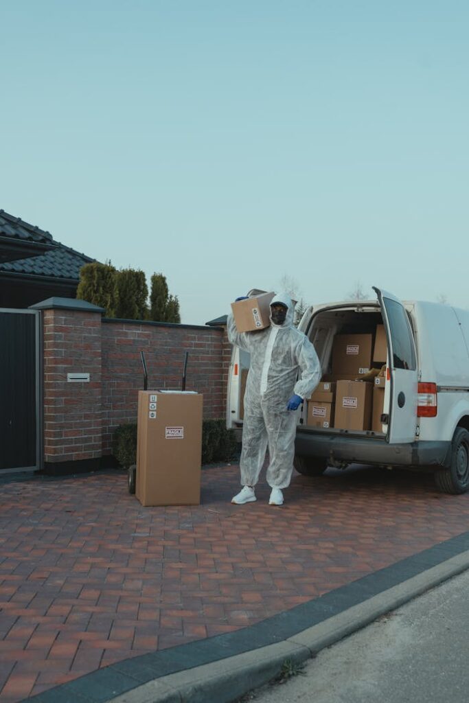 photo 6170465 A delivery person in protective gear unloading packages from a van outdoors.