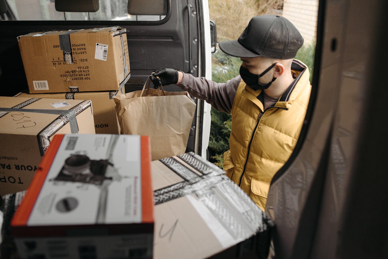 gallery-04 A masked deliveryman loads packages into a van, illustrating modern logistics.