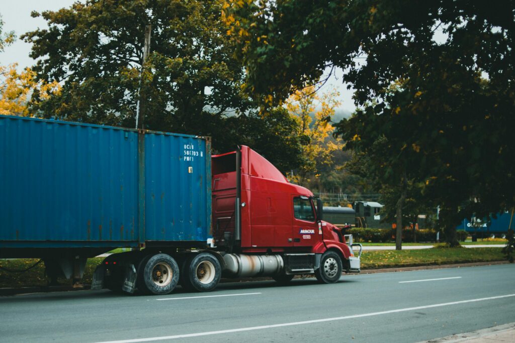 A red truck transports a blue cargo container on a scenic, tree-lined road. A red truck transports a blue cargo container on a scenic, tree-lined road.